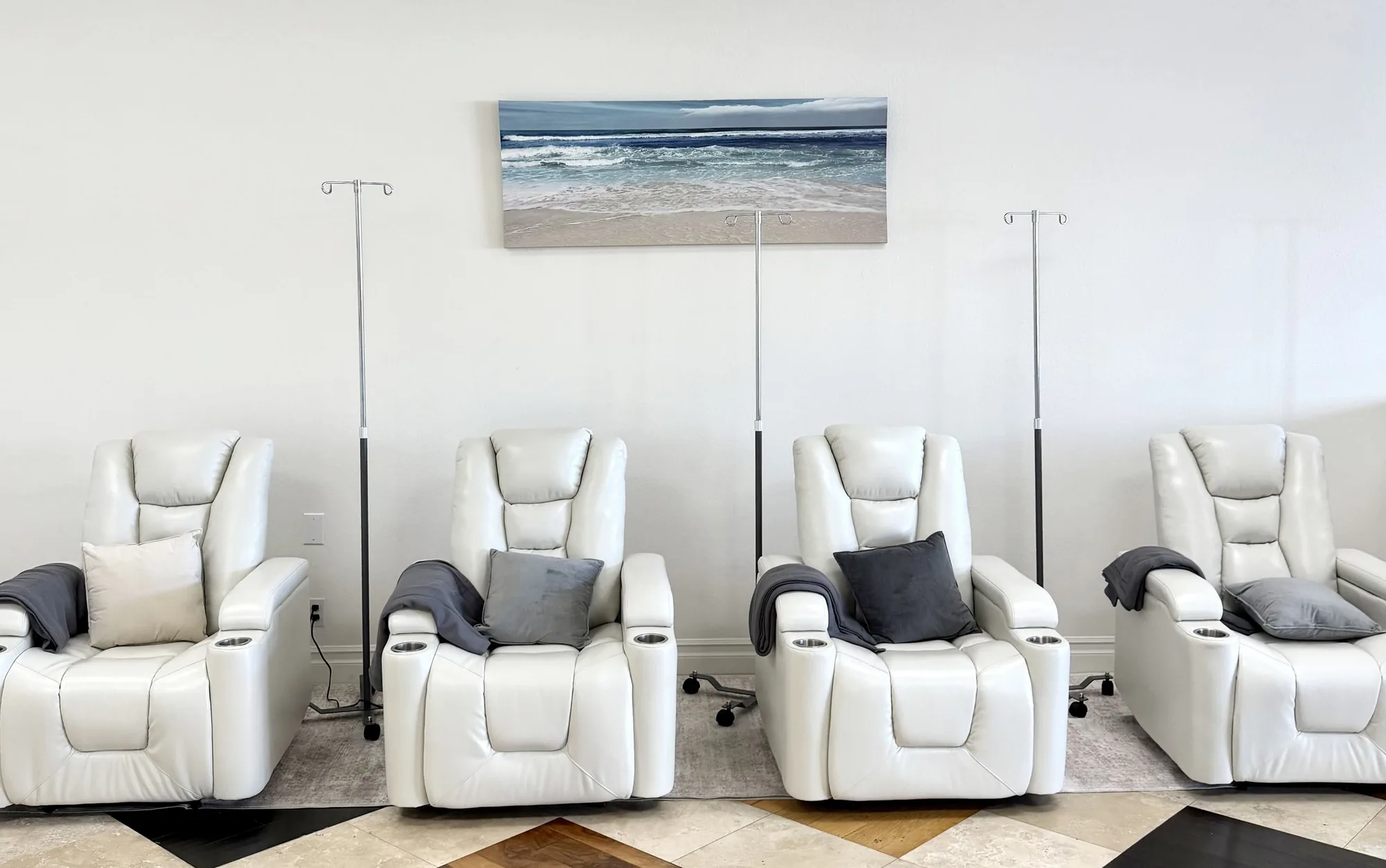 Four white leather recliners with IV stands beneath an ocean painting in the Epic IV lounge